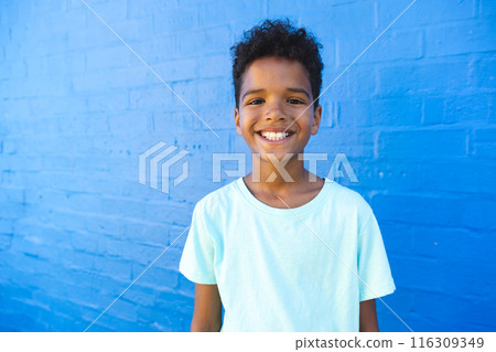 Biracial boy smiles brightly against a blue wall 116309349