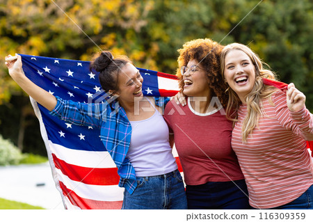 Happy diverse female friends covered with flag of usa in garden 116309359