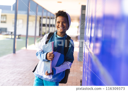 Smiling biracial boy stands by school lockers, with copy space Smiling biracial boy stands by school lockers, with copy space 116309373