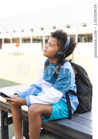 Biracial boy enjoys music outdoors at school, with copy space 116309434