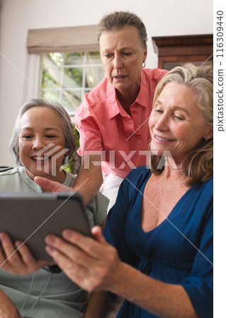 Diverse senior female friends sharing tablet at home, all smiling together Diverse senior female friends sharing tablet at home, all smiling together 116309440