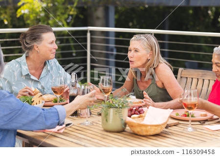 Diverse senior female friends enjoying meal outdoors, chatting and laughing Diverse senior female friends enjoying meal outdoors, chatting and laughing 116309458