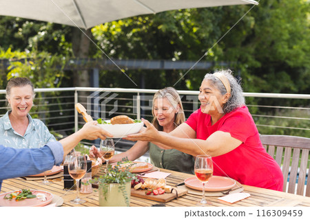 Diverse senior female friends sharing meal outdoors, passing dishes Diverse senior female friends sharing meal outdoors, passing dishes 116309459