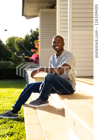 Young African American man sitting on steps outside home, smiling at camera Young African American man sitting on steps outside home, smiling at camera 116309489