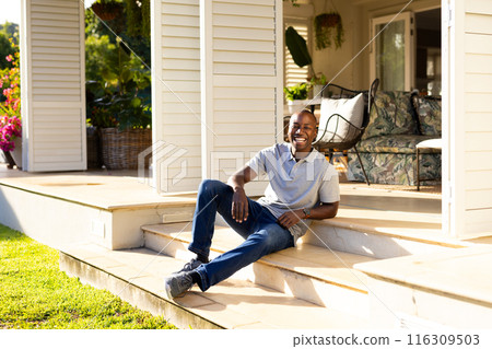 Outdoors, young African American man sitting on steps smiling at camera on sunny day Outdoors, young African American man sitting on steps smiling at camera on sunny day 116309503