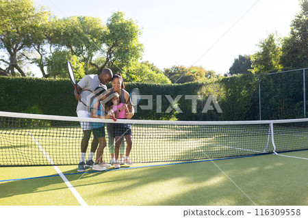 Outdoors, diverse family of four enjoying game of tennis together on outdoor court 116309558