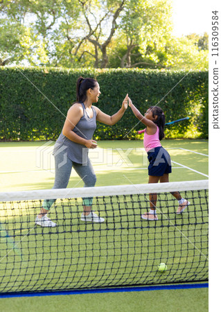 Outdoors, biracial mother and daughter giving high-five on tennis court Outdoors, biracial mother and daughter giving high-five on tennis court 116309584