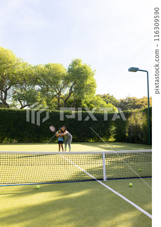 Outdoors, biracial mother and daughter learning tennis on court 116309590