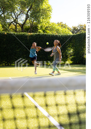 Outdoors, biracial mother and daughter playing tennis together on a court Outdoors, biracial mother and daughter playing tennis together on a court 116309593