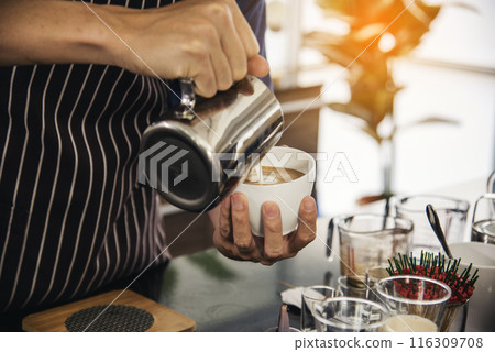 Coffee barista pour espresso shot and make latte art hot coffee cup. Cappuccino with milk in italian coffee shop cafe. Close up hands of barista make brown latte art for customer cafeteria. 116309708