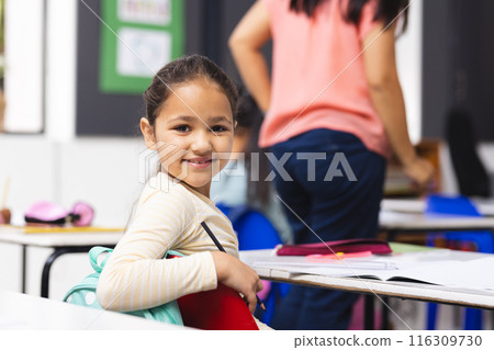 Biracial girl sitting at desk in classroom, smiling at camera 116309730