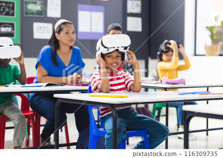 Biracial female teacher and children using VR sets in classroom 116309735