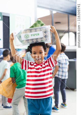 An African American child smiles holding recycling bin labeled Paper over his head 116309741