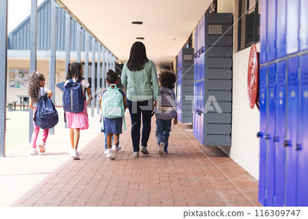 A biracial teacher walking with students in school hallway with blue lockers A biracial teacher walking with students in school hallway with blue lockers 116309747
