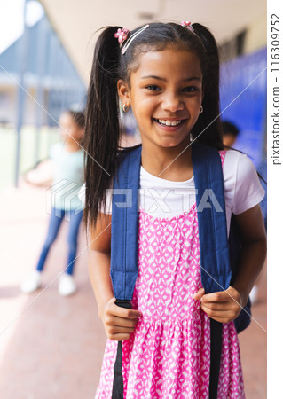 Biracial girl wearing pink dress and backpack smiling at school Biracial girl wearing pink dress and backpack smiling at school 116309752