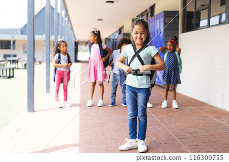 Biracial students standing outside school building, wearing backpacks and smiling 116309755