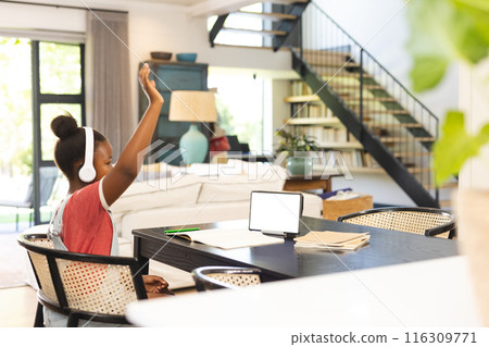 Young African American girl wearing headphones raising hand while studying on tablet, copy space 116309771