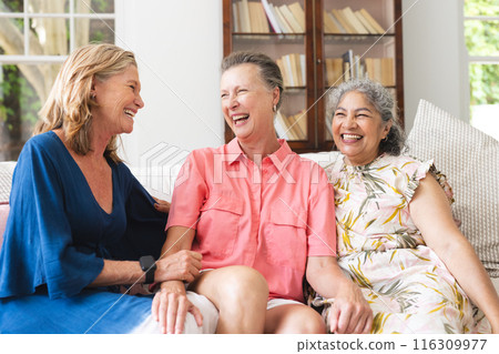 Diverse, mature women sitting together, smiling in living room at home Diverse, mature women sitting together, smiling in living room at home 116309977
