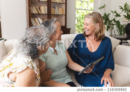 Diverse group of senior women friends using tablet at home on sofa Diverse group of senior women friends using tablet at home on sofa 116309982