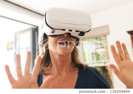 Senior caucasian woman using virtual reality headset, at home 116309994