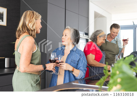 Diverse group of mature women enjoying wine and conversation in modern kitchen 116310018