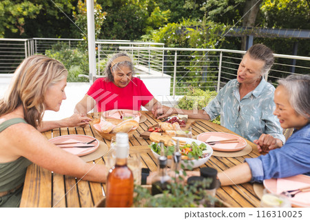 A diverse senior women saying grace before meal outdoors, smiling A diverse senior women saying grace before meal outdoors, smiling 116310025