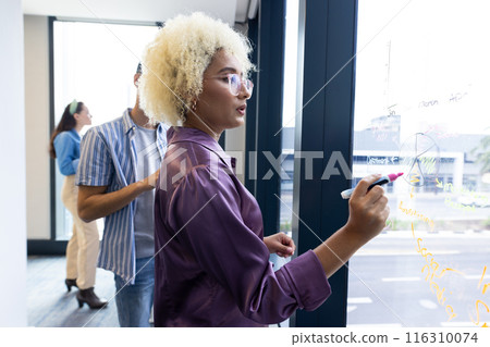 Biracial woman writing on window, business, brainstorming 116310074