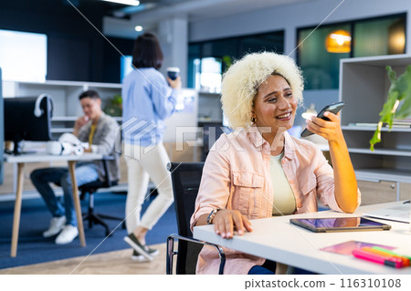 Biracial woman smiling while talking on smartphone in modern business office 116310108