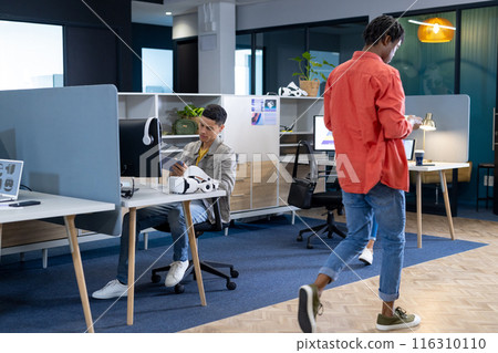 A biracial man sits at a desk, looking at his smartphone in a modern office A biracial man sits at a desk, looking at his smartphone in a modern office 116310110