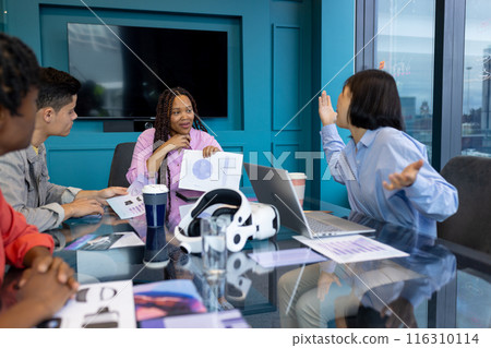 Diverse Business colleagues use a laptop and VR headset to review documents in a startup meeting 116310114