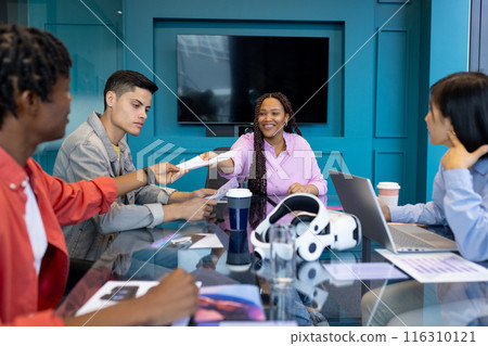 Colleagues gather as biracial woman hands document to man at a startup 116310121