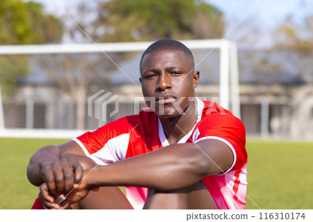 Young African American soccer player sitting on soccer field, looking focused 116310174
