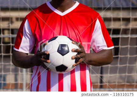 African American soccer player holding soccer ball, wearing red and white jersey 116310175
