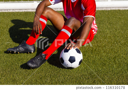 African American soccer player sitting on grass holding soccer ball 116310178