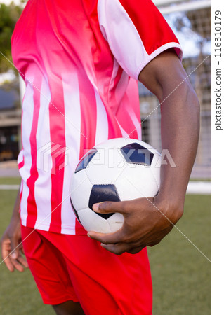African American soccer player holds soccer ball, wears red and white sports uniform African American soccer player holds soccer ball, wears red and white sports uniform 116310179
