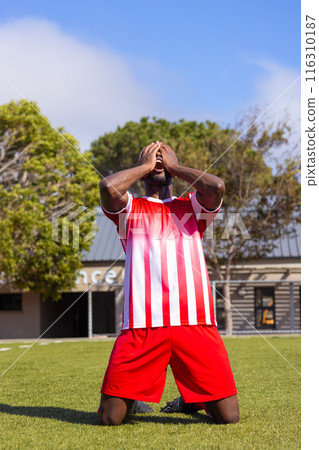 African American soccer player kneeling on grass, appearing emotional African American soccer player kneeling on grass, appearing emotional 116310187