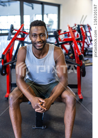 Strong African American man sits on gym bench, smiling confidently after working out 116310197