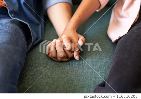 Diverse couple holding hands on green couch, showing affection 116310203