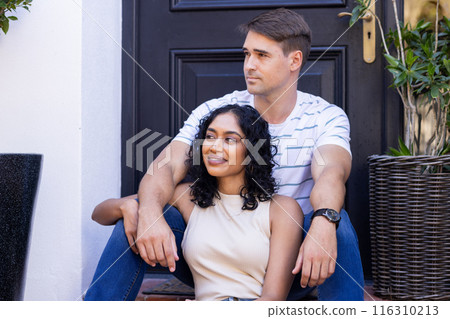 Diverse couple sitting together on steps, looking content 116310213