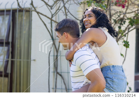 Young Caucasian man giving Asian woman piggyback ride, both smiling and having fun 116310214