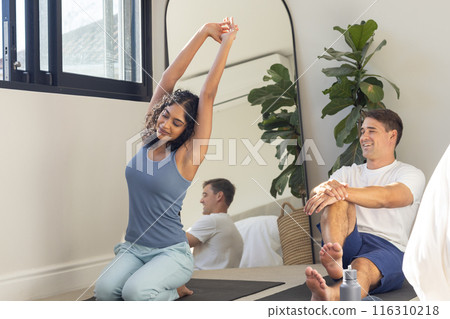 Young diverse couple practicing yoga together at home in bright room Young diverse couple practicing yoga together at home in bright room 116310218