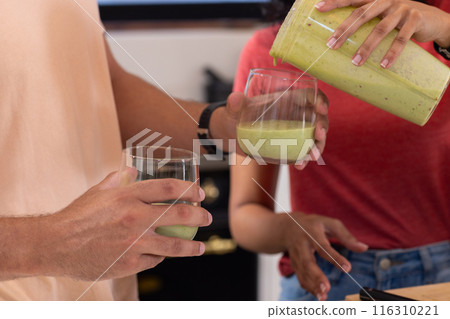 Diverse couple pouring green smoothies into glasses Diverse couple pouring green smoothies into glasses 116310221