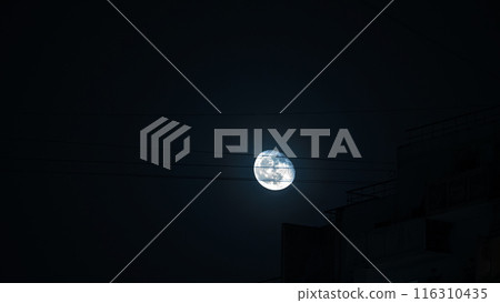 Night city scene with full bright moon against dark blue sky and electric wires. The atmosphere is mysterious and serene. Night city scene with full bright moon against dark blue sky and electric wires. The atmosphere is mysterious and serene. 116310435