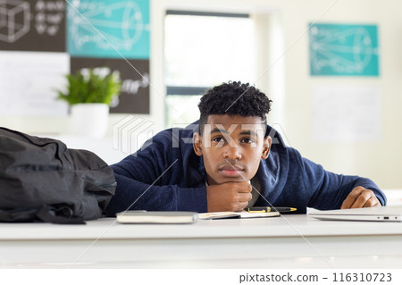 In school, African American teenage boy resting head on desk, looking thoughtful 116310723