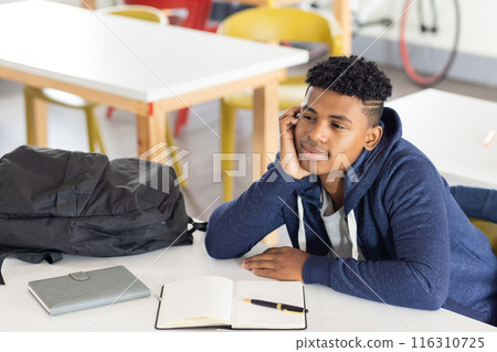 In school, African American male student daydreaming at desk with notebook and pen, copy space 116310725