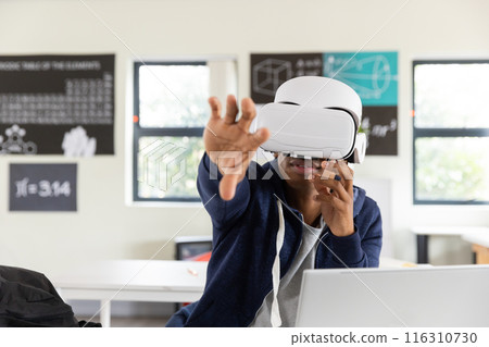 In school, African American male student using VR headset and reaching out in classroom 116310730