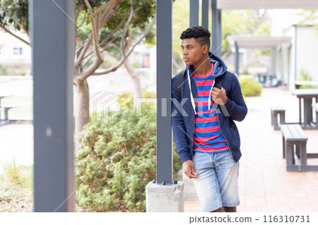 Walking outdoors, African American male student wearing backpack, looking away thoughtfully, copy sp 116310731