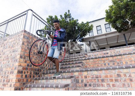 Carrying bicycle down stairs, African American male student in casual clothes outdoors, copy space Carrying bicycle down stairs, African American male student in casual clothes outdoors, copy space 116310736