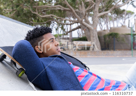 Relaxing at skatepark, teenage boy lying on skateboard, enjoying leisure time 116310737