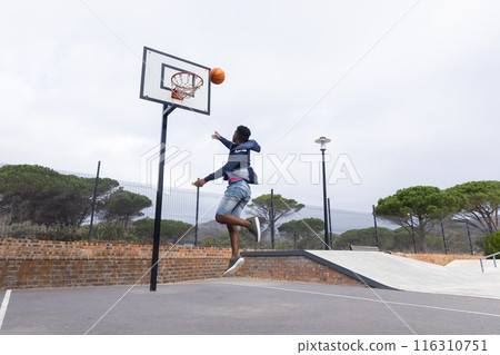 Playing basketball, teenage boy jumping to dunk ball at outdoor court, copy space Playing basketball, teenage boy jumping to dunk ball at outdoor court, copy space 116310751